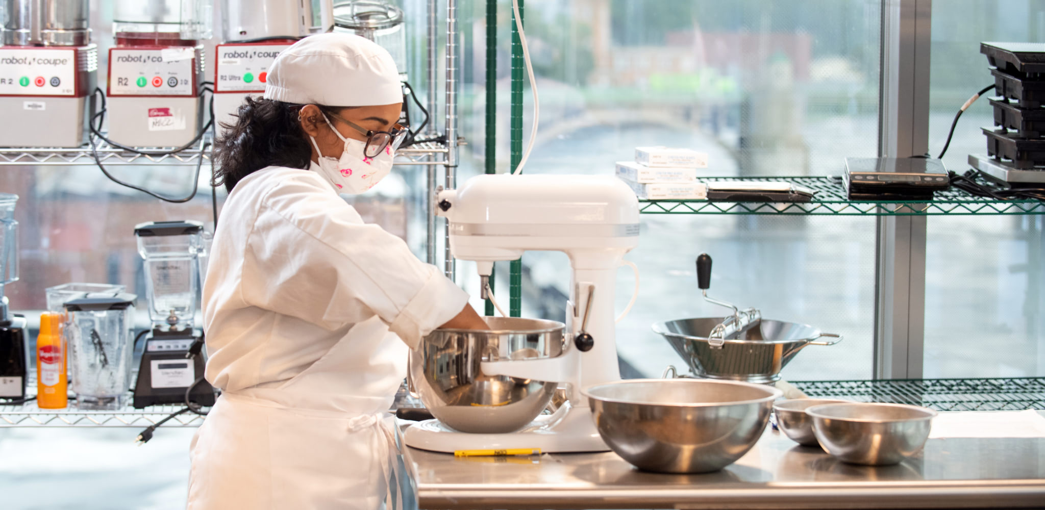 A Culinary Arts Certificate student uses a standing mixer while preparing a meal in class.