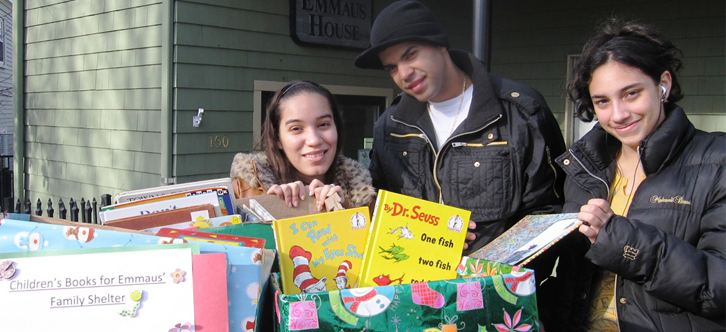 Three NECC students at Emmaus House with several large boxes of children's books.