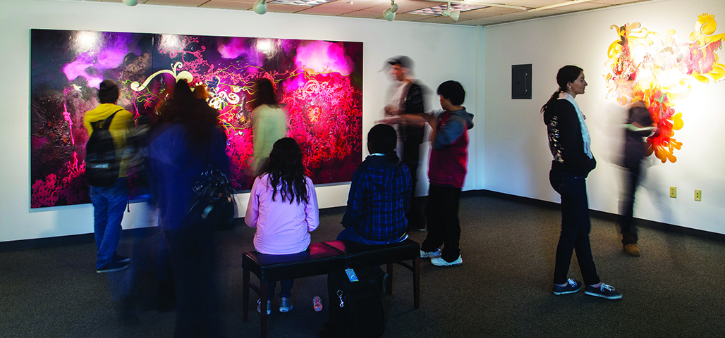Several people gather around a large coloful painting hanging on a wall in the artspace.