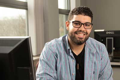 Junior De Los Santos Galan sits in front of a computer.