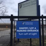 Large blue sign on the fence saying "Dimitry / Lot A Parking Entrance. Turn Left at Light".