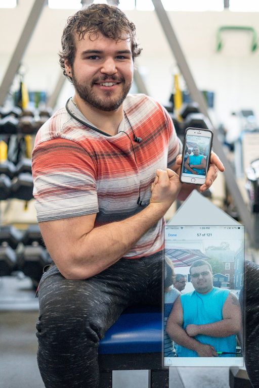 Adam Kinser, in the wellness center gym, holding up his phone with an image on it of himself when he weighed more.