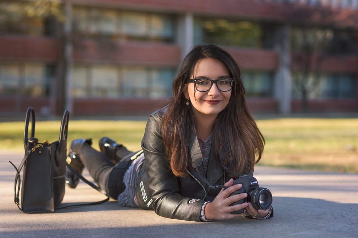 Alejandra Chandler, lying on her stomache on the sidewalk, taking a photograph with a DSL camera.