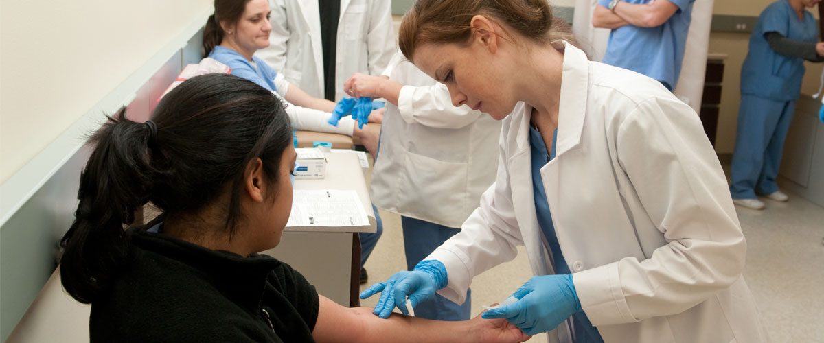 A Healthcare Technician Certificate student inspects the arm of a mock patient.
