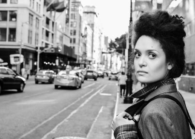 Black and white historic-like imagery or Diannely on a sidewalk of a busy street in the city.