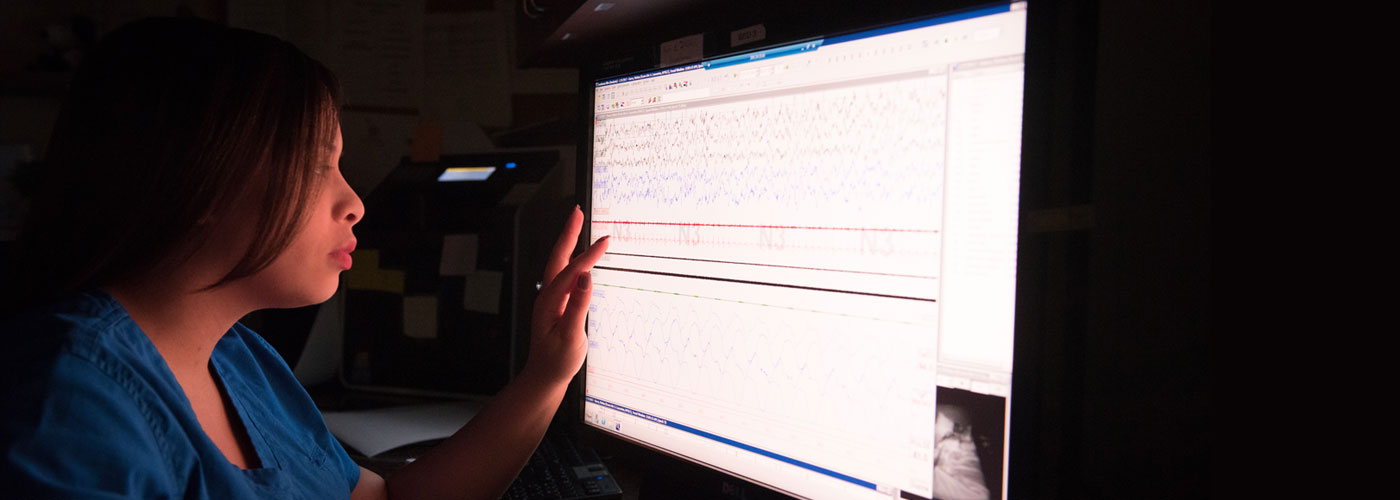 A student in the Sleep Technology Certificate program examines sleep patterns on a screen in a dark room.