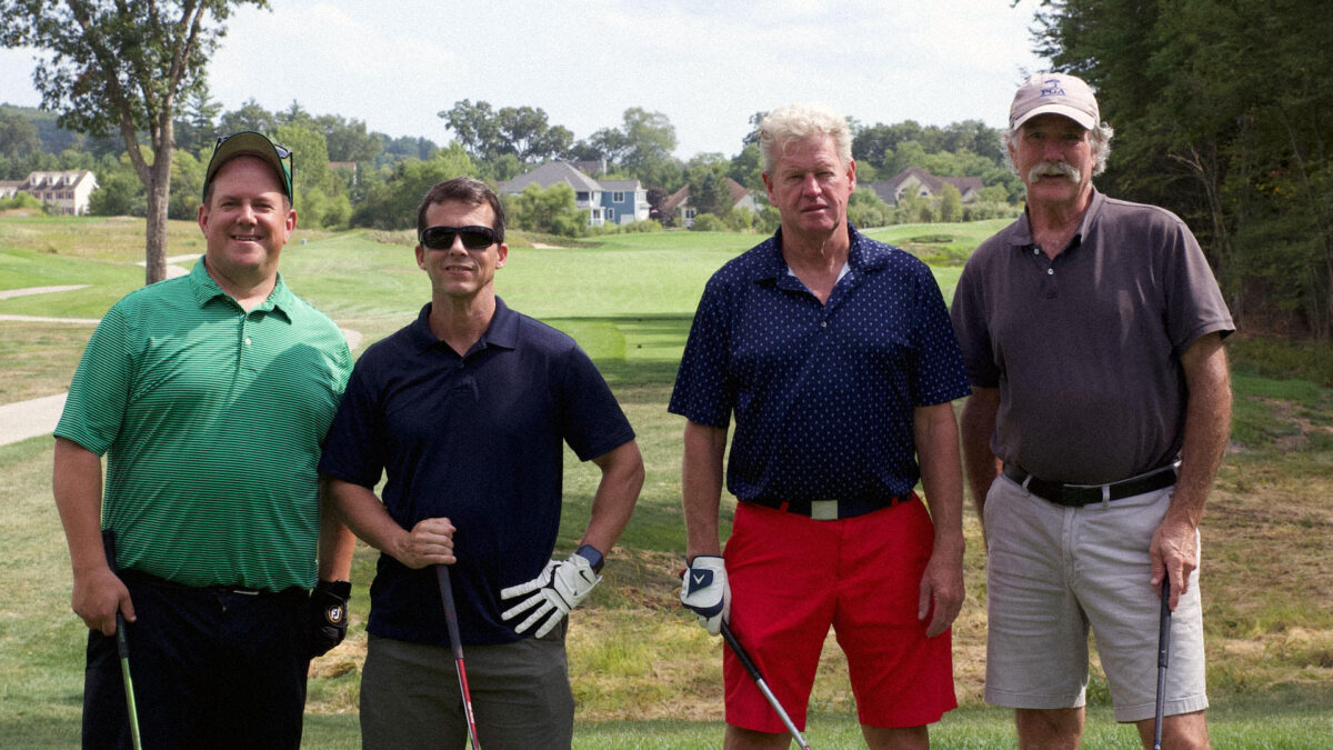 Photo of four male presenting golfers standing outside in front of a field
