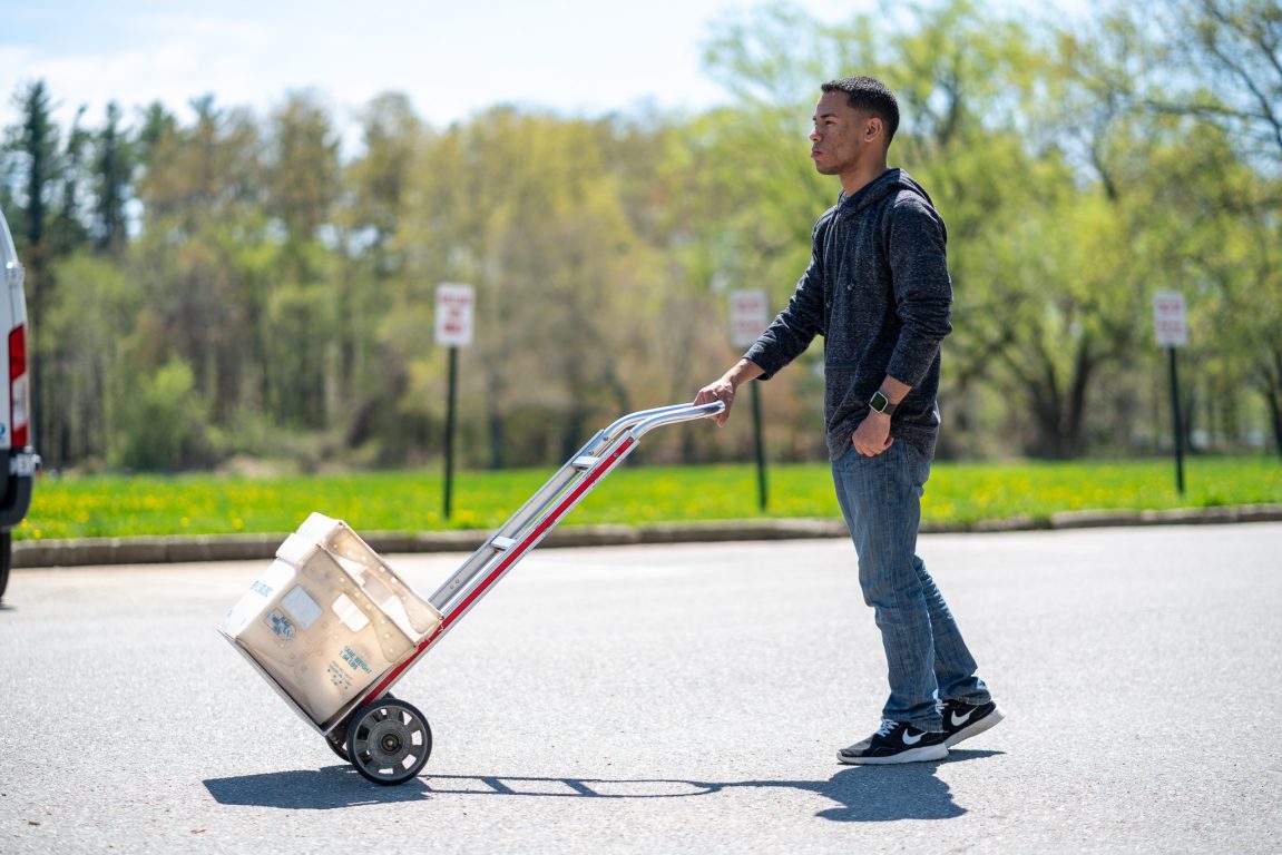 Peter Rodriguez, pushing a hand cart with a box of mail on it.