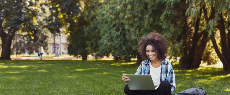 Smiling woman sitting in front of computer outside.