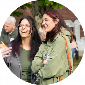 Photo of two female students on the NECC campus in conversation with someone out of frame and smiling