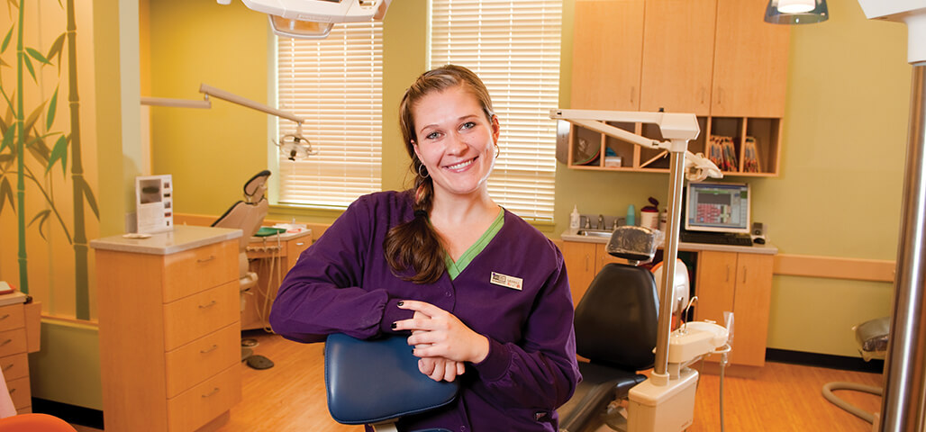 A student in the Dental Assisting Certificate program sits in the chair in a mock dental office room