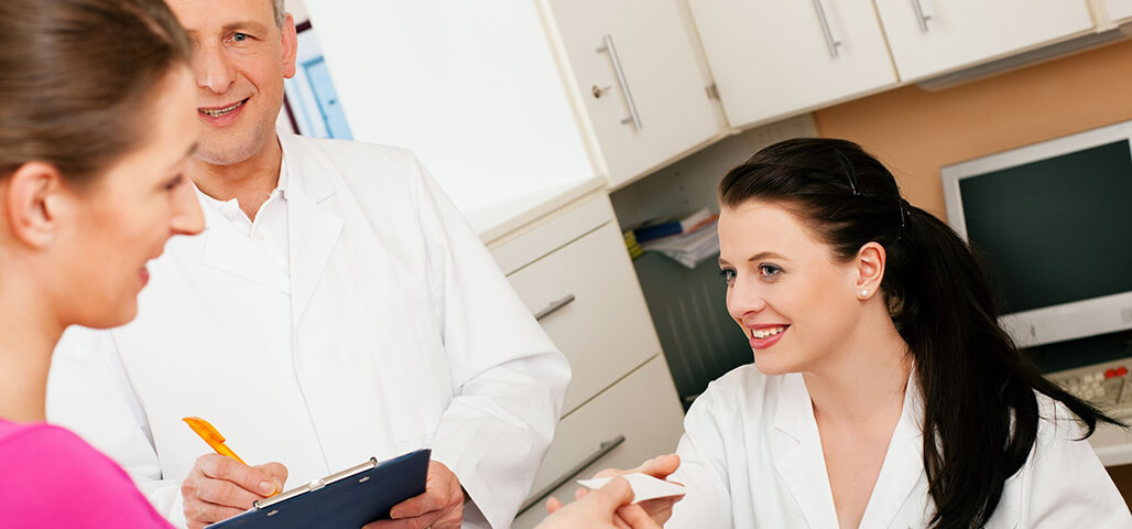 Two medical office assistants students helping a patient at the desk in the office.