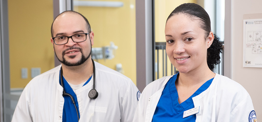 Two nursing students, one male, one female stand next to each other smiling.