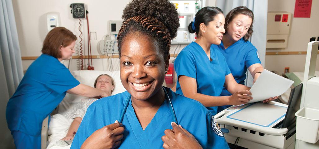 Four Practical Nursing Certificate students in a simulation hospital room with a 'patient' on the bed.