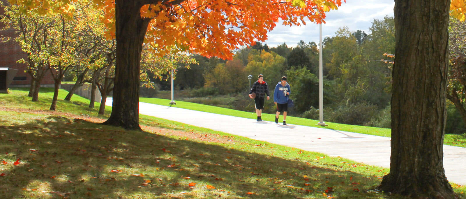 A photo of two students walking across the Haverhill campus in the middle of the fall, with autumn leaves in the foreground