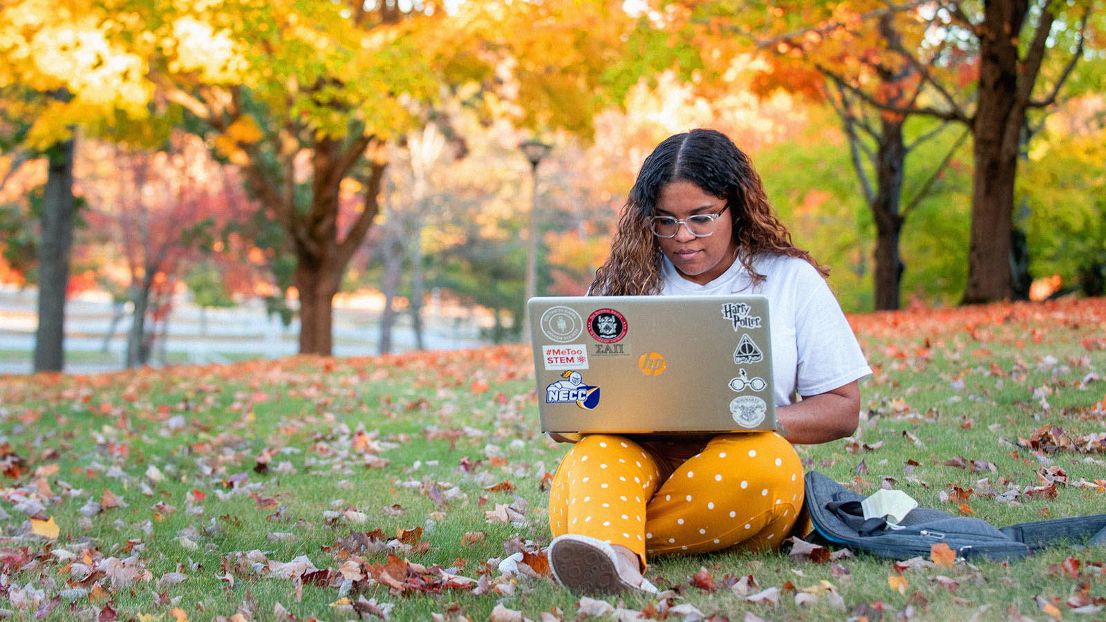 Woman sitting outside on the NECC campus with a laptop in the Fall