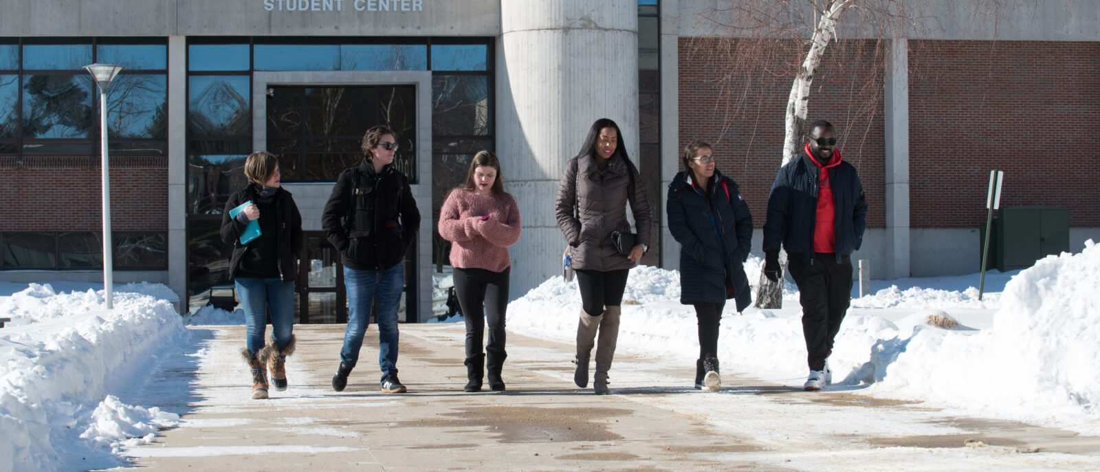 A photo of a group of students walking outside on the Haverhill campus, wearing winter jackets, walking with snow banks all around them through a cleared path