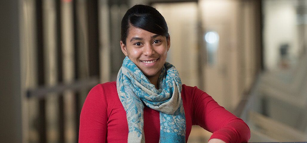 A young woman in the Liberal Arts: Psychology degree program, leaning her arm on a table and smiling.