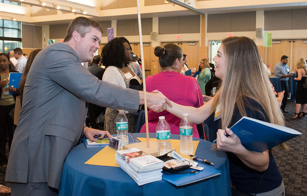 A young woman shakes hands with a business partner at a table.