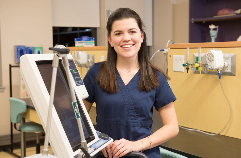 A female presenting health student standing in front of equipment, smiling at the camera