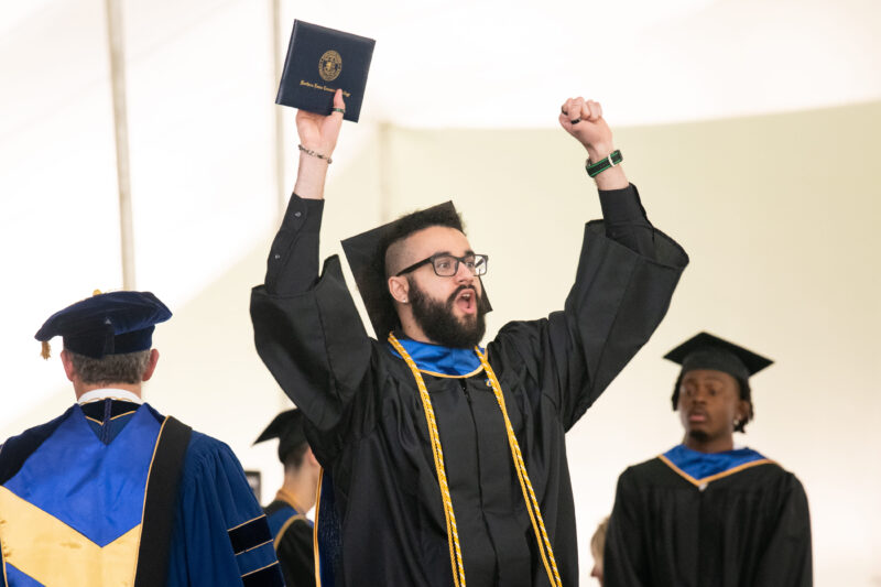 a student cheering at commencement with a diploma