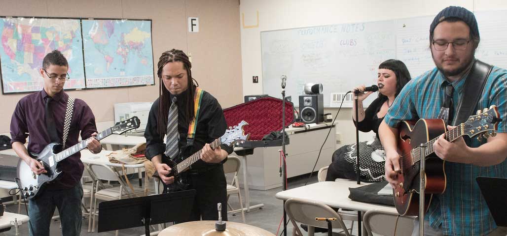 Group of 4 students in NECC Music Degree program, playing music instruments and singing in a classroom.