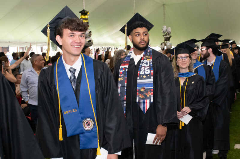 A photo of two male presenting graduating students, standing in the crowd during the Commencement 2025 ceremony