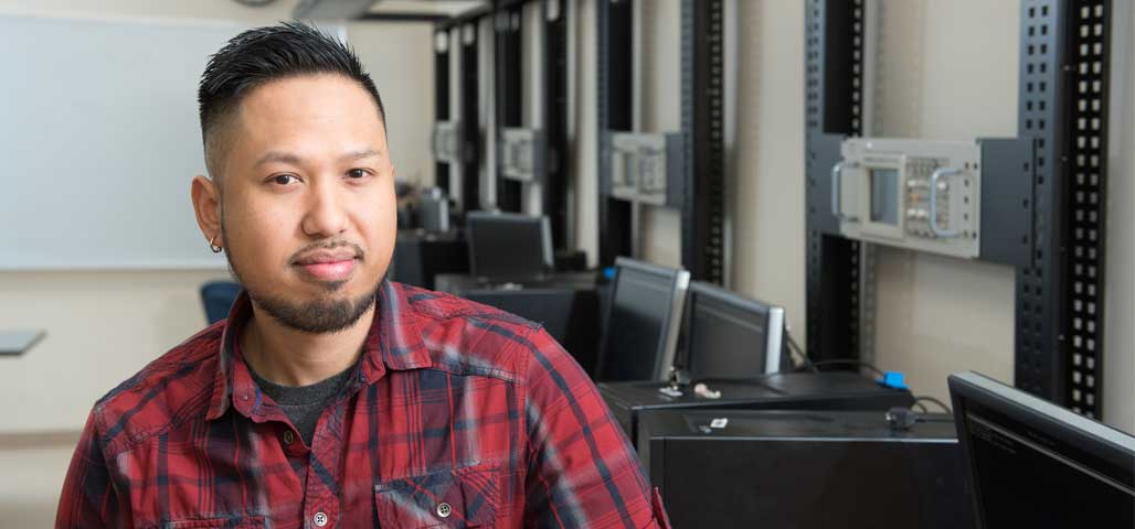 A student in the Test B Electronic Equipment Technology Certificate program in a computer lab surrounded by equipment..